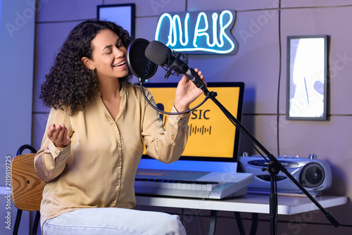Bild auf Leinwand Young African-American woman with microphone singing at table in recording studi