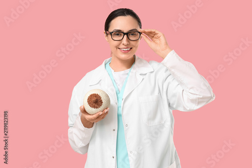 Female doctor with knitted breast model on pink background