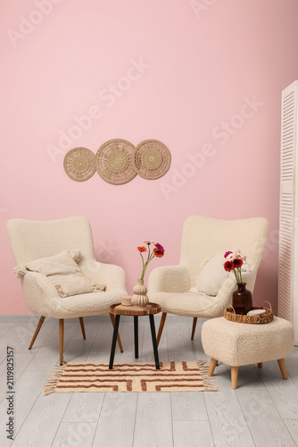 Armchairs, pouf and coffee table with gerbera flowers in vase in interior of ...