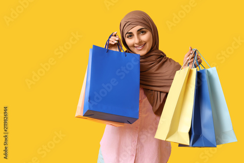Beautiful Muslim woman with shopping bags on yellow background
