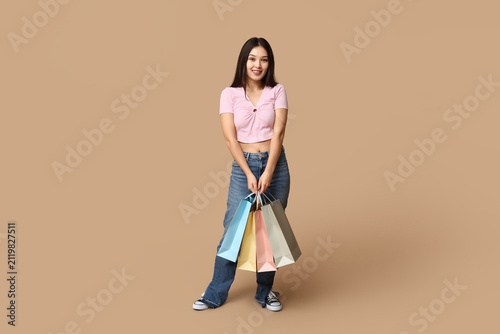Fashionable young Asian woman in stylish jeans with shopping bags on brown ba...