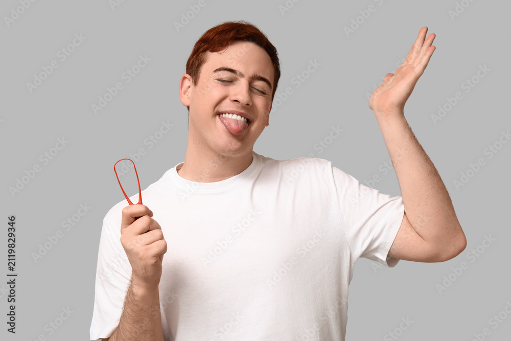 Fototapeta premium Young man with tongue scraper on grey background