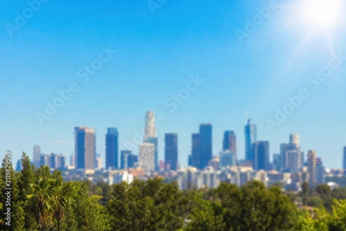 Modern skyline with futuristic skyscrapers glowing under bright blue sky, vibrant urban cityscape framed by lush green tropical foliage, aerial-inspired perspective