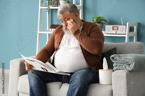 Portrait of sad senior man on sofa reading newspaper in living room