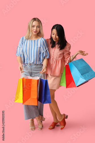 Beautiful young women with shopping bags on pink background