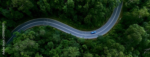 aerial view of a winding asphalt road cutting through dense green forest. Scenic mountain roadway surrounded by lush tropical trees, ideal for travel, transportation, nature, adventure, sustainability