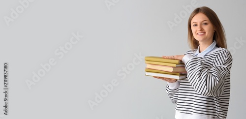 Smiling young female student holding a stack of textbooks, education and lear...