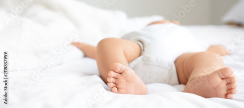 Canvas Print Newborn baby's tiny feet and legs on a soft white bed, childhood innocence and c