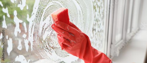 Obraz na płótnie Person in red rubber glove cleaning a window with a sponge and soapy foam, home
