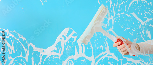 Canvastavla Hand holding a squeegee cleaning a window with soap suds and foam on a bright bl