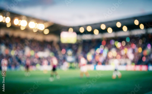A blurred image of a soccer match in a stadium, showing players and spectators in a vibrant atmosphere during a game, capturing the excitement of the sport.