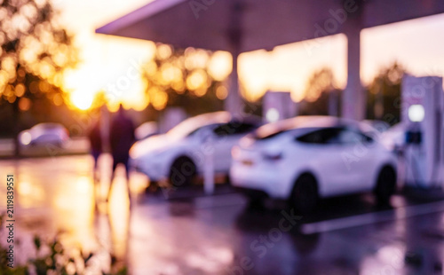 A blurred image capturing the ambiance of an electric vehicle charging station during sunset, highlighting modern electric cars and charging infrastructure.