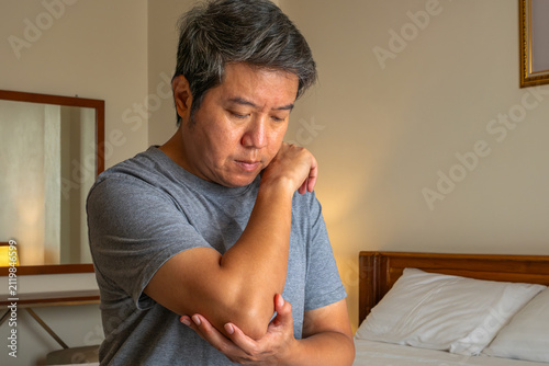 Photography Man holding elbow in discomfort, symbolizing joint pain and medical treatment focus