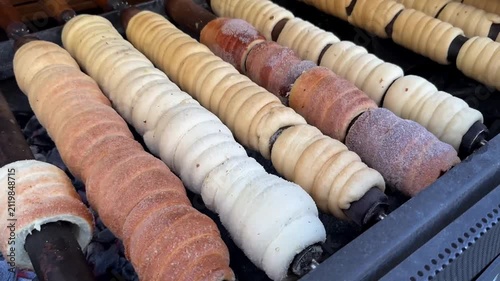 Baking traditional Trdelnik chimney cakes rotating on spit over hot embers, close-up