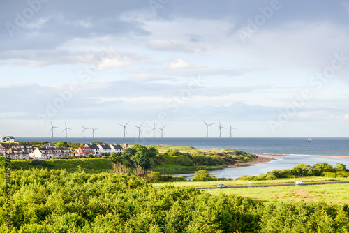 Scenic coastal landscape with offshore wind turbines, green countryside, seaside homes and dramatic clouds along the North Sea coast near Aberdeen, Scotland