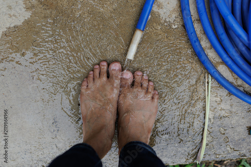 Bare feet washing under a stream of fresh water from a blue hosepipe on concrete, showcasing personal hygiene, refreshing sensations, and simple outdoor cleanliness