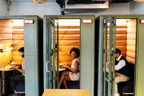 Diverse individuals focusing on tasks inside contemporary coworking space privacy pods, ensuring concentration and productivity in an open office environment