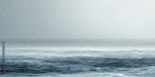 Calm mist ocean waves under a hazy overcast  horizon grey sky in soft blue monochromatic sea waters, minimal seascape