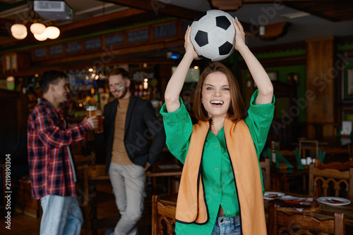 Konstfotografi Woman exuberantly elevates football above her head amidst jovial gathering with