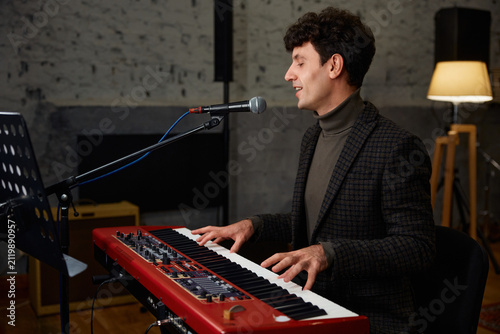 Musician crafting melodies. Performer engages with synthesizer in studio setting