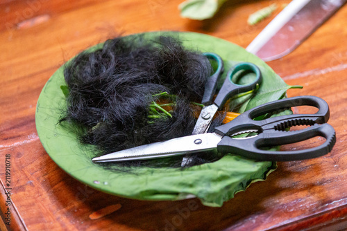 Obraz na płótnie Cut black hair and scissors placed on a green leaf during a traditional ordination ceremony