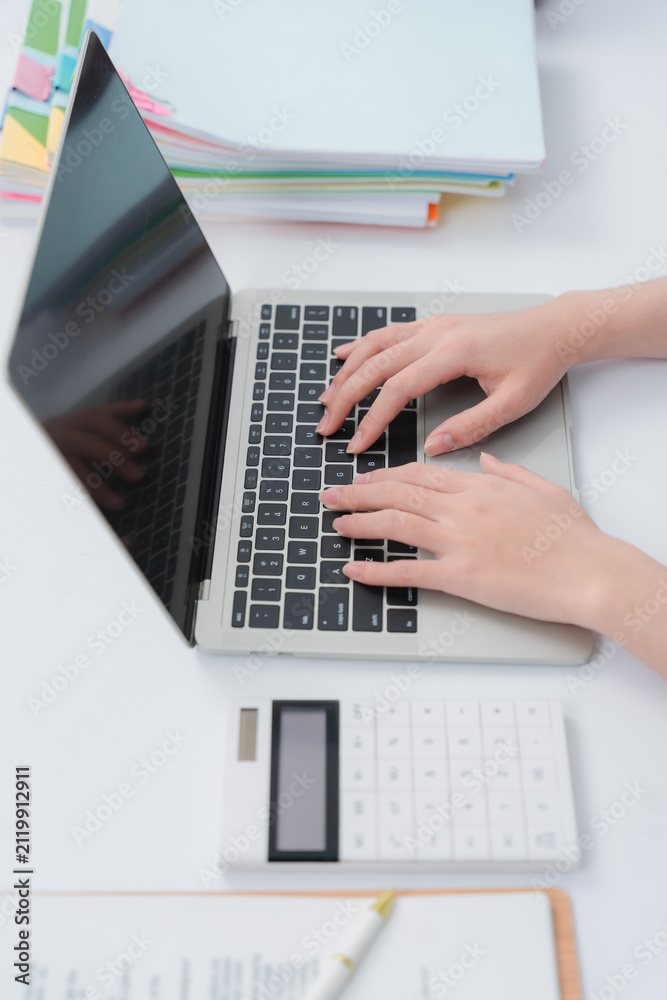 Fototapeta premium Hands typing on a laptop beside a calculator and documents, indicating productive work.