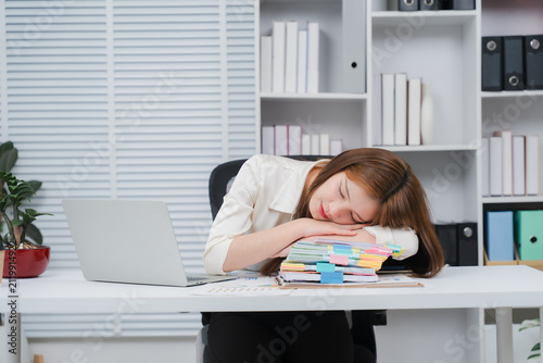 Quadro su tela Exhausted Employee Sleeping at Desk: A young businesswoman slumps asleep on a stack of paperwork on her office desk, overwhelmed by workload, with a laptop nearby