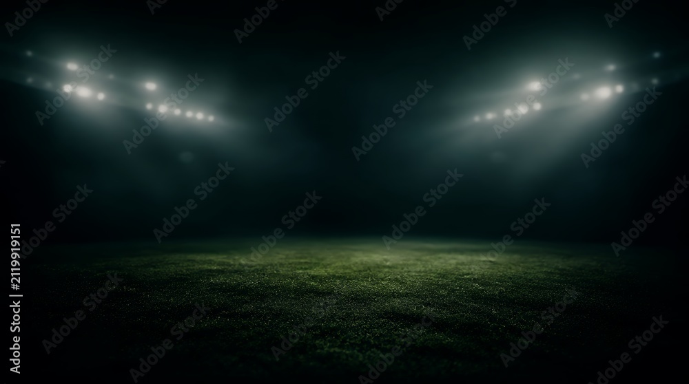 Naklejka premium Empty dark stadium field illuminated by bright floodlights at night.