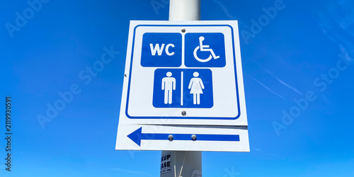 Close-up of a blue and white French public toilet direction sign with an arrow and accessibility pictogram