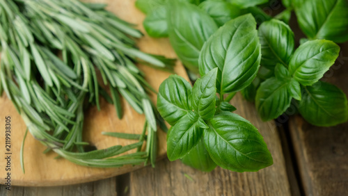Basil leaves and rosemary sprigs on wooden board. Fresh herbs background, seasoning.