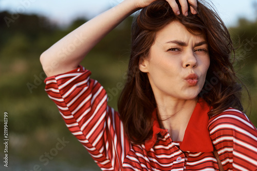 Obraz na plátne Young brunette woman in a red striped shirt poses playfully outdoors, pouting her lips towards the camera during a golden hour sunset to capture a fun and authentic candid moment