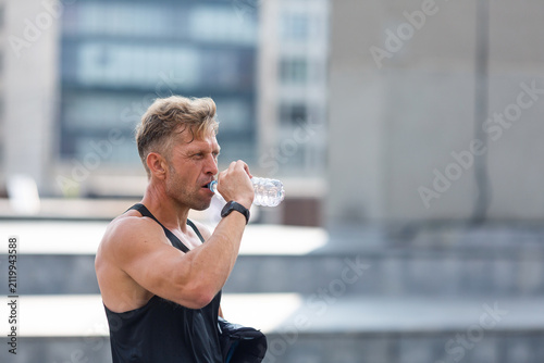 A middle-aged man drinks water after a roller hockey practice on an asphalt rink.