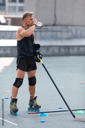 A middle-aged man drinks water after a roller hockey practice on an asphalt rink
