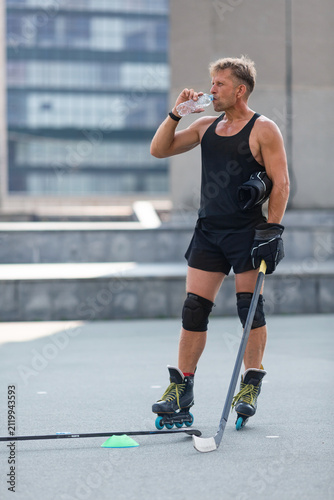 A man pauses after a roller hockey practice to hydrate with clean water from a plastic bottle.