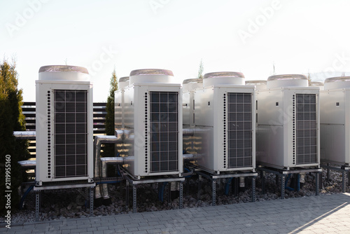 Multiple external industrial AC compressors and heat pumps installed outside a commercial building. Modern HVAC system, central air conditioning, and ventilation equipment concept.