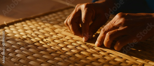 Close-up of artisan hands weaving a traditional bamboo mat. Skilled worker crafting natural fibers using manual basketry techniques. Sustainable handicraft concept for artisan marketing campaigns.