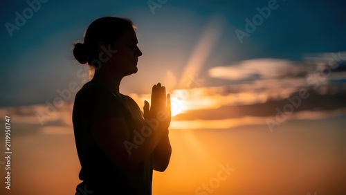 Woman silhouette practicing meditation in sunset light