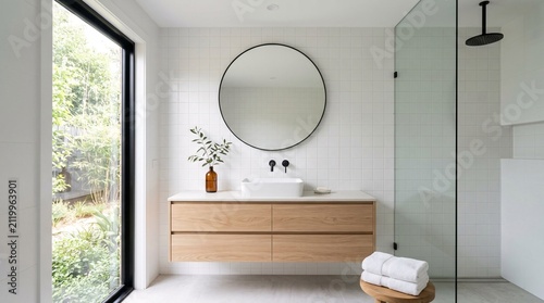 Foto Modern bathroom with wooden vanity and large round mirror on tiled wall
