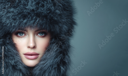 Woman in a fur hat poses with a serious expression in front of a plain gray background