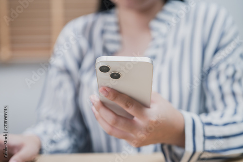 Close up of a business woman holding a smartphone while working in a modern home office. Mobile technology, online communication
