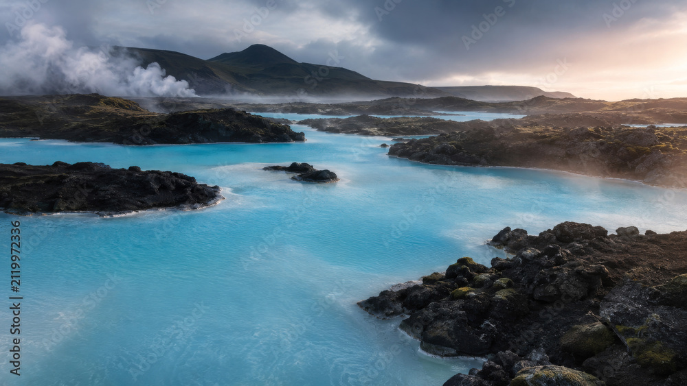 Fototapeta premium Turquoise Geothermal Lagoon With Steam Rising Off Dark Volcanic Rock Formation Landscape