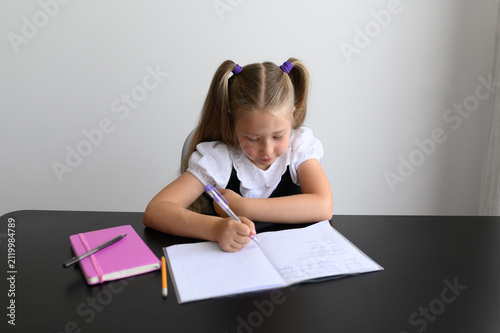 Foto Diligent girl focused on writing in copybook sitting at dark desk