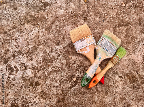 Bild auf Leinwand Three used Paintbrushes with wooden handles arranged diagonally on dirty concrete surface