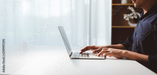 Person typing on modern laptop keyboard, engaging in professional work remotely, writing email, coding, or learning online in a bright home office setting