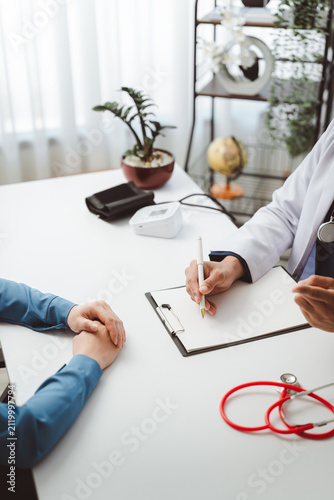 Doctor discussing patient history and health examination, medical professional recording data during consultation, providing care and treatment plan