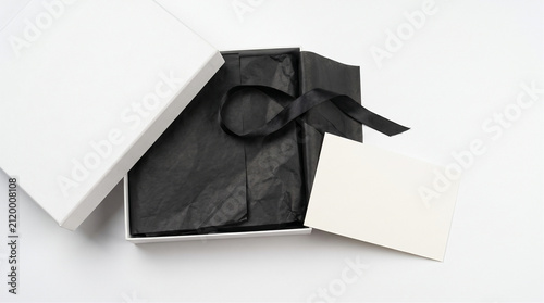 Top view of luxury open white gift box mockup with black tissue paper, satin ribbon and blank greeting card on white background