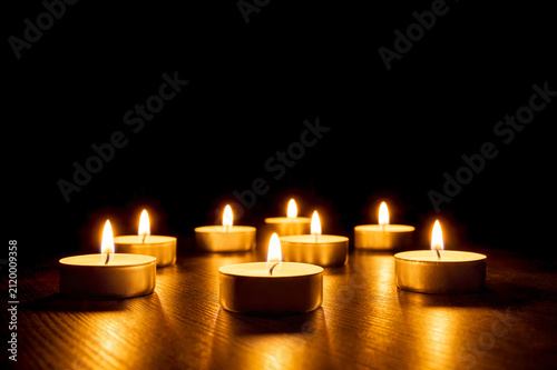 Fotografie Group of tealight candles burning on black background