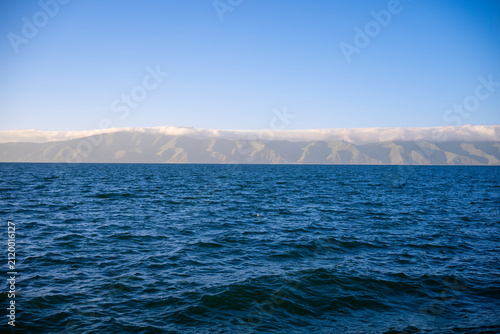 Deep Blue Wavy Water Surface looking towards Distant Foggy Mountain Range