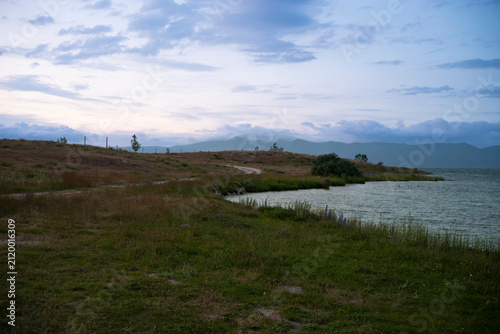 Tranquil Lake Shore at Twilight with Distant Misty Mountains and Overcast Sky
