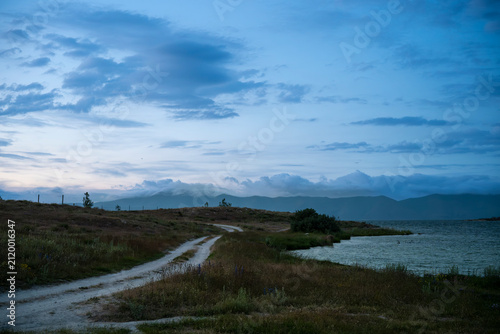 Winding Dirt Road along Coastal Lake in Twilight with Clouds over Mountains